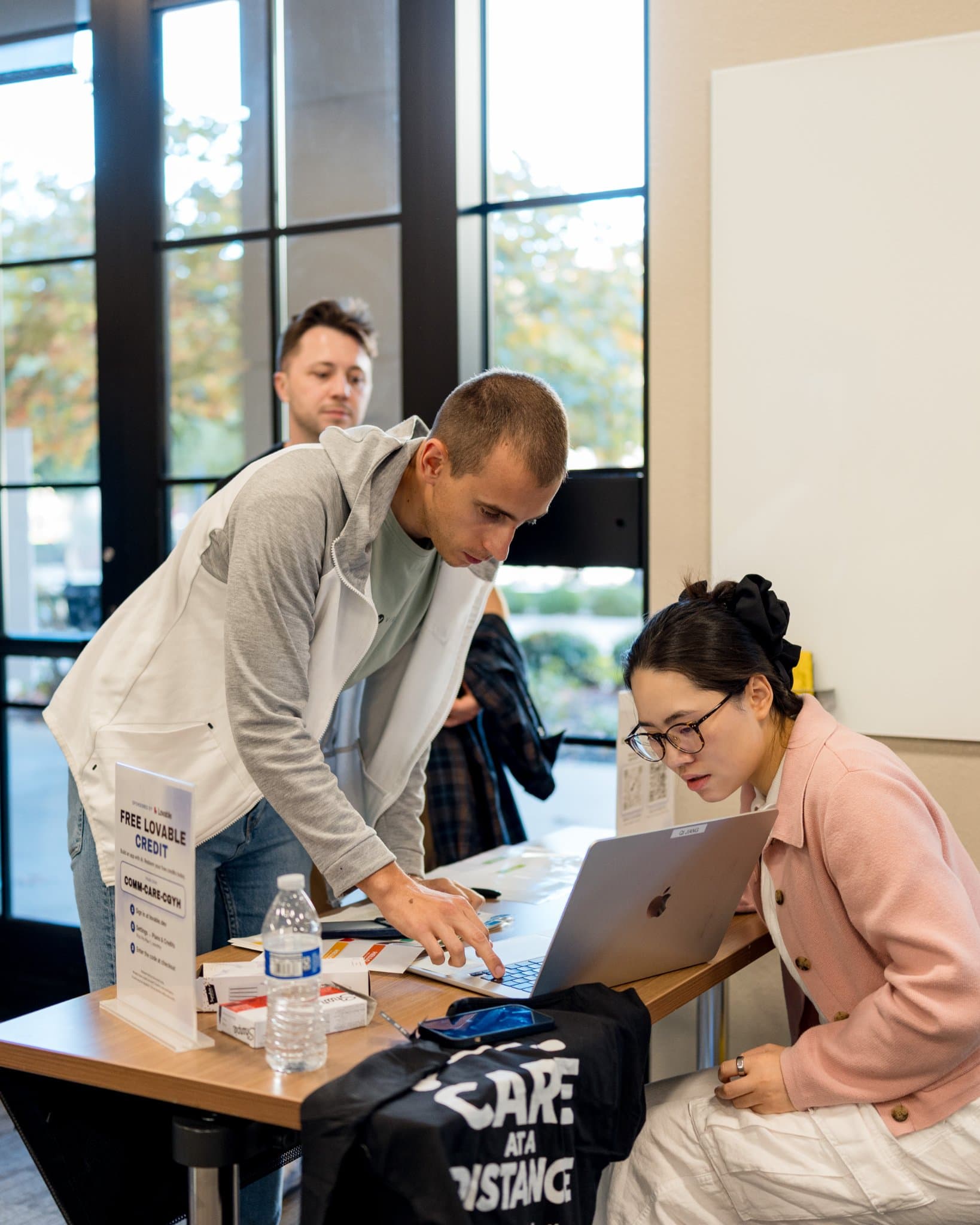 Vertical shot of an attendee signing in at the registration table beside Care at a Distance T-shirts at Care at a Distance: AI, Sensors, Robotics and the Future of Aging, SF Tech Week 2026 at EVGR, Stanford University by JY Studio