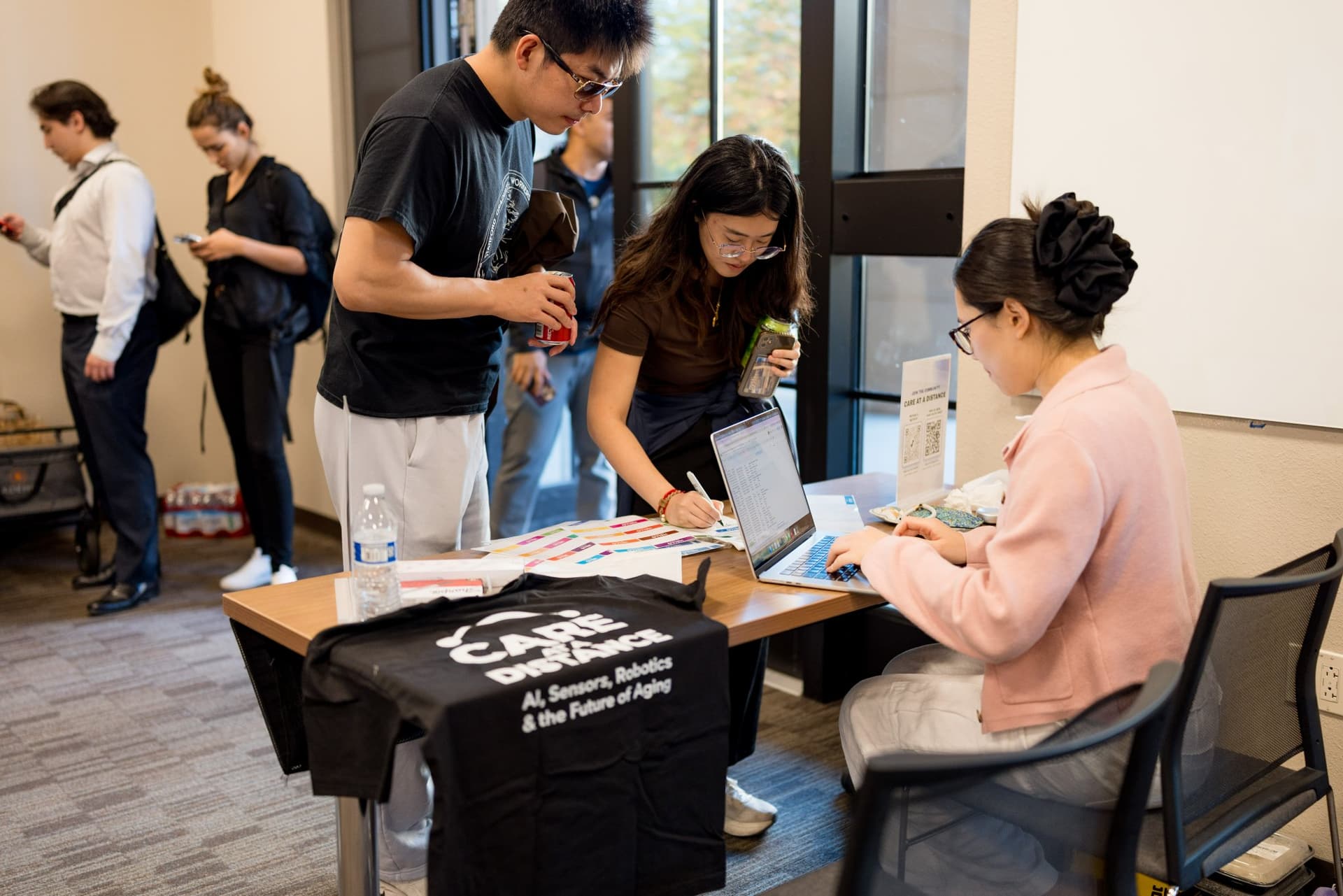 Check-in table with Care at a Distance "AI, Sensors, Robotics & the Future of Aging" T-shirts at Care at a Distance: AI, Sensors, Robotics and the Future of Aging, SF Tech Week 2026 at EVGR, Stanford University by JY Studio