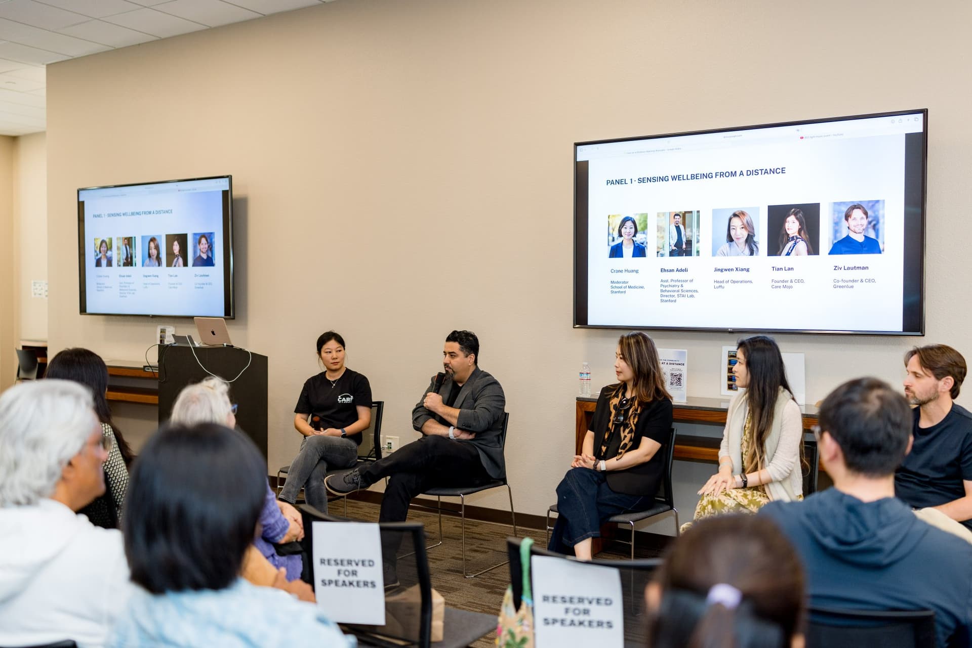 Wide view of Panel 1 "Sensing Wellbeing from a Distance" with the panel slide on both screens at Care at a Distance: AI, Sensors, Robotics and the Future of Aging, SF Tech Week 2026 at EVGR, Stanford University by JY Studio