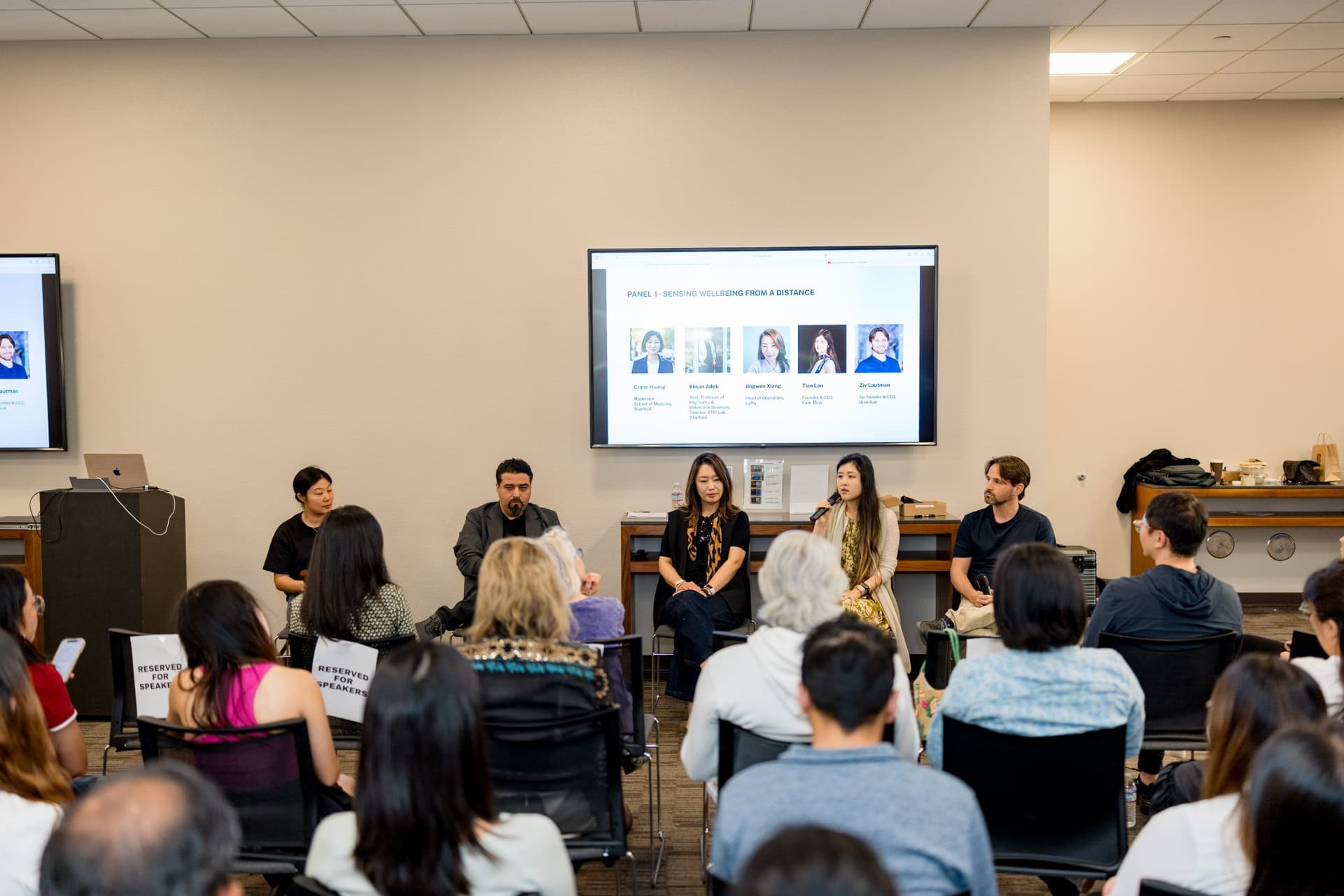 Panel 1 "Sensing Wellbeing from a Distance" speakers seated in front of a full audience at Care at a Distance: AI, Sensors, Robotics and the Future of Aging, SF Tech Week 2026 at EVGR, Stanford University by JY Studio