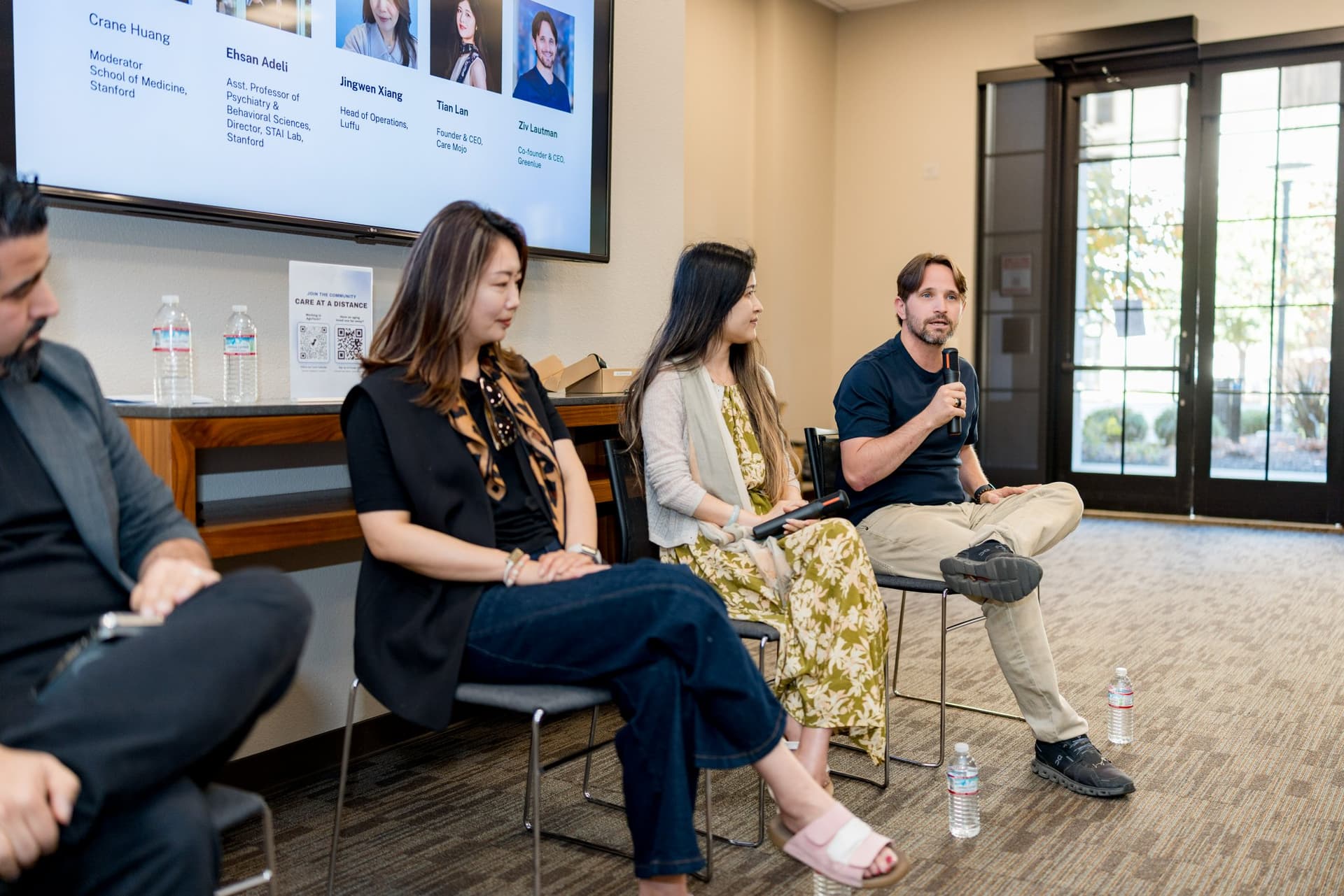 Three panelists of Panel 1 "Sensing Wellbeing from a Distance" in conversation by the windows at Care at a Distance: AI, Sensors, Robotics and the Future of Aging, SF Tech Week 2026 at EVGR, Stanford University by JY Studio