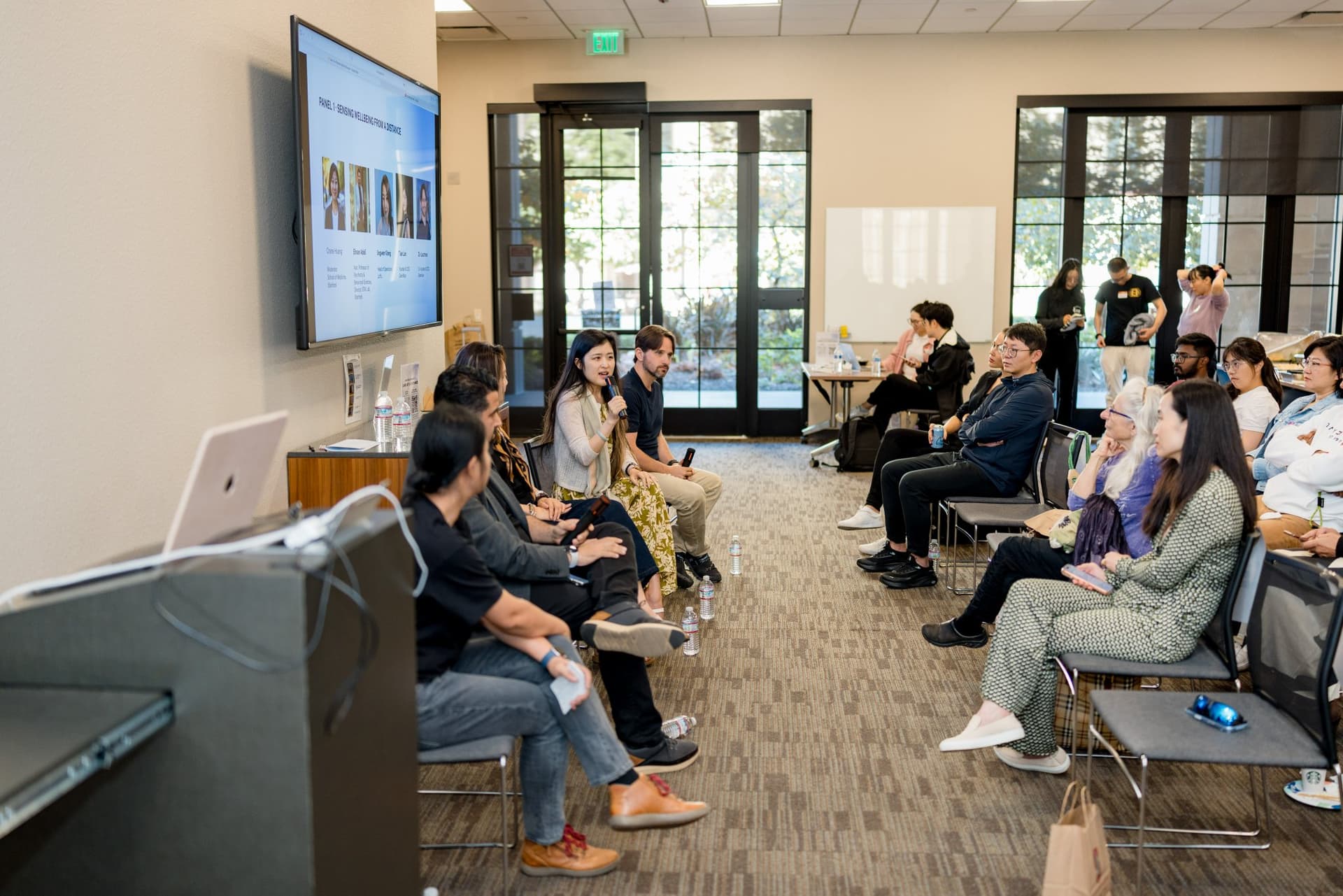 Side view of the Panel 1 "Sensing Wellbeing from a Distance" panelists and front-row audience at Care at a Distance: AI, Sensors, Robotics and the Future of Aging, SF Tech Week 2026 at EVGR, Stanford University by JY Studio