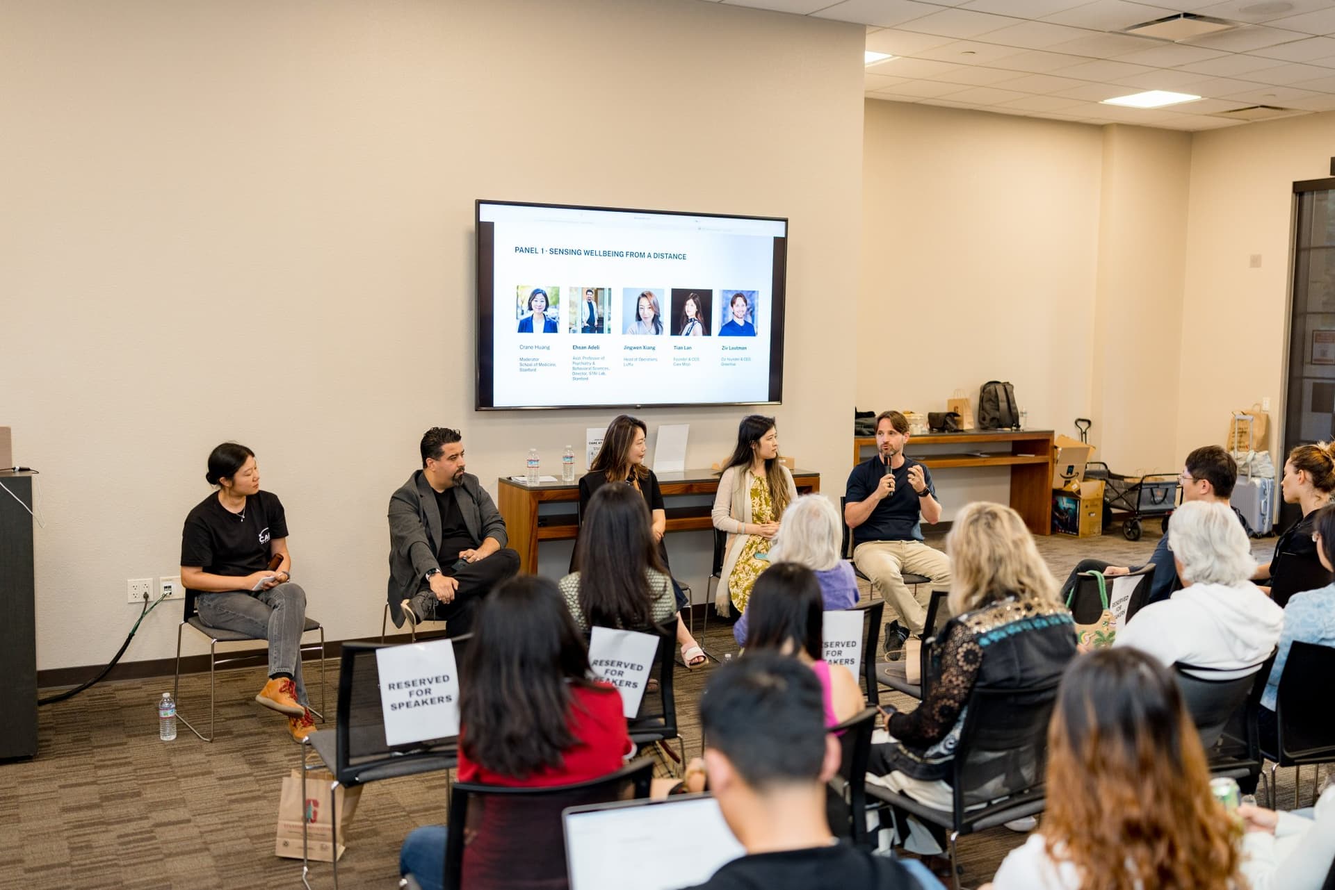 Wide shot of the Panel 1 "Sensing Wellbeing from a Distance" panel and audience at Care at a Distance: AI, Sensors, Robotics and the Future of Aging, SF Tech Week 2026 at EVGR, Stanford University by JY Studio