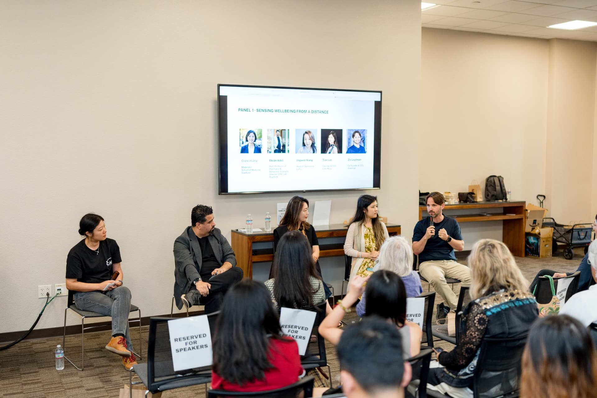 Moderator and four panelists of Panel 1 "Sensing Wellbeing from a Distance" in front of a full room at Care at a Distance: AI, Sensors, Robotics and the Future of Aging, SF Tech Week 2026 at EVGR, Stanford University by JY Studio