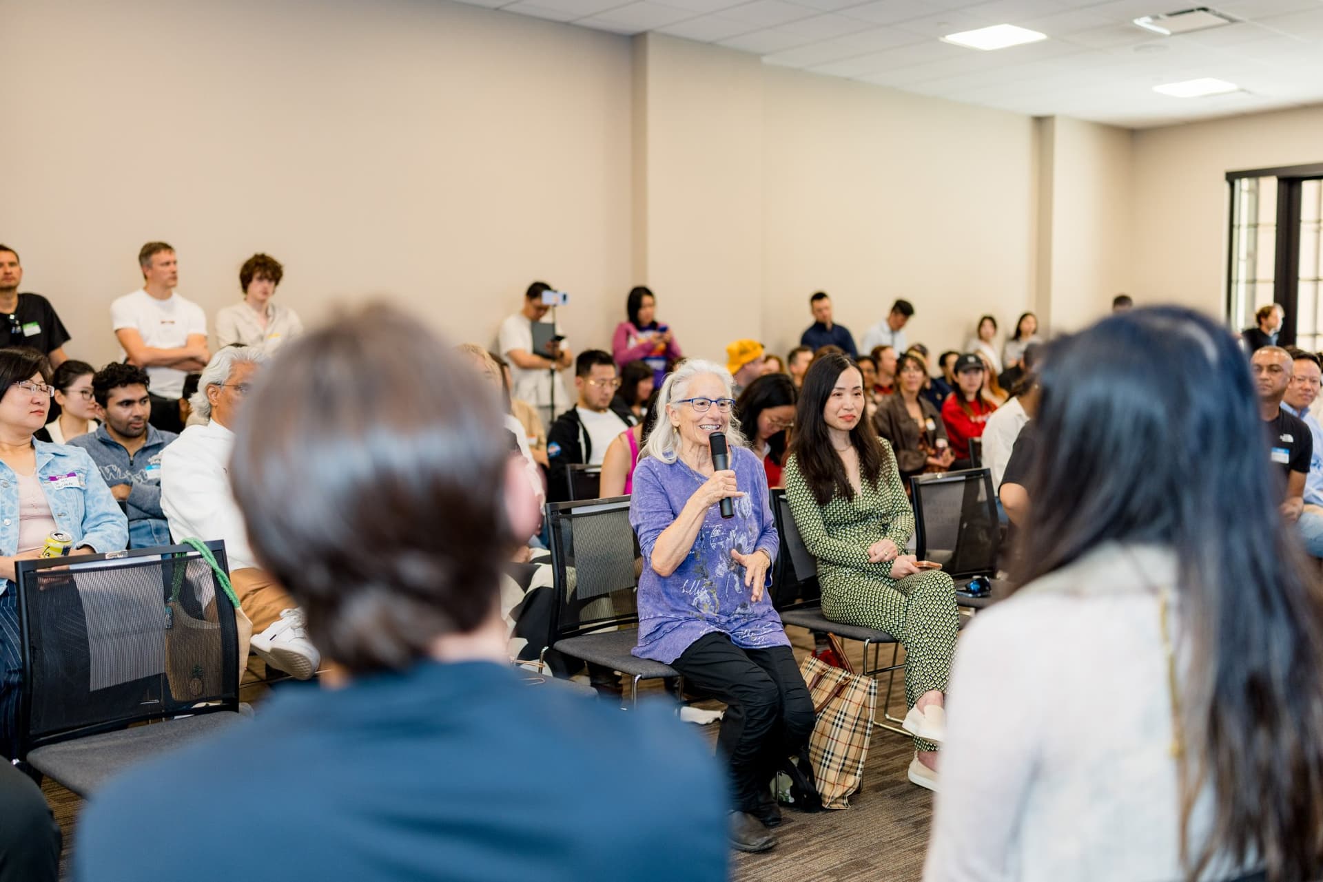 Attendee asking the panel a question with a microphone during audience Q&A at Care at a Distance: AI, Sensors, Robotics and the Future of Aging, SF Tech Week 2026 at EVGR, Stanford University by JY Studio