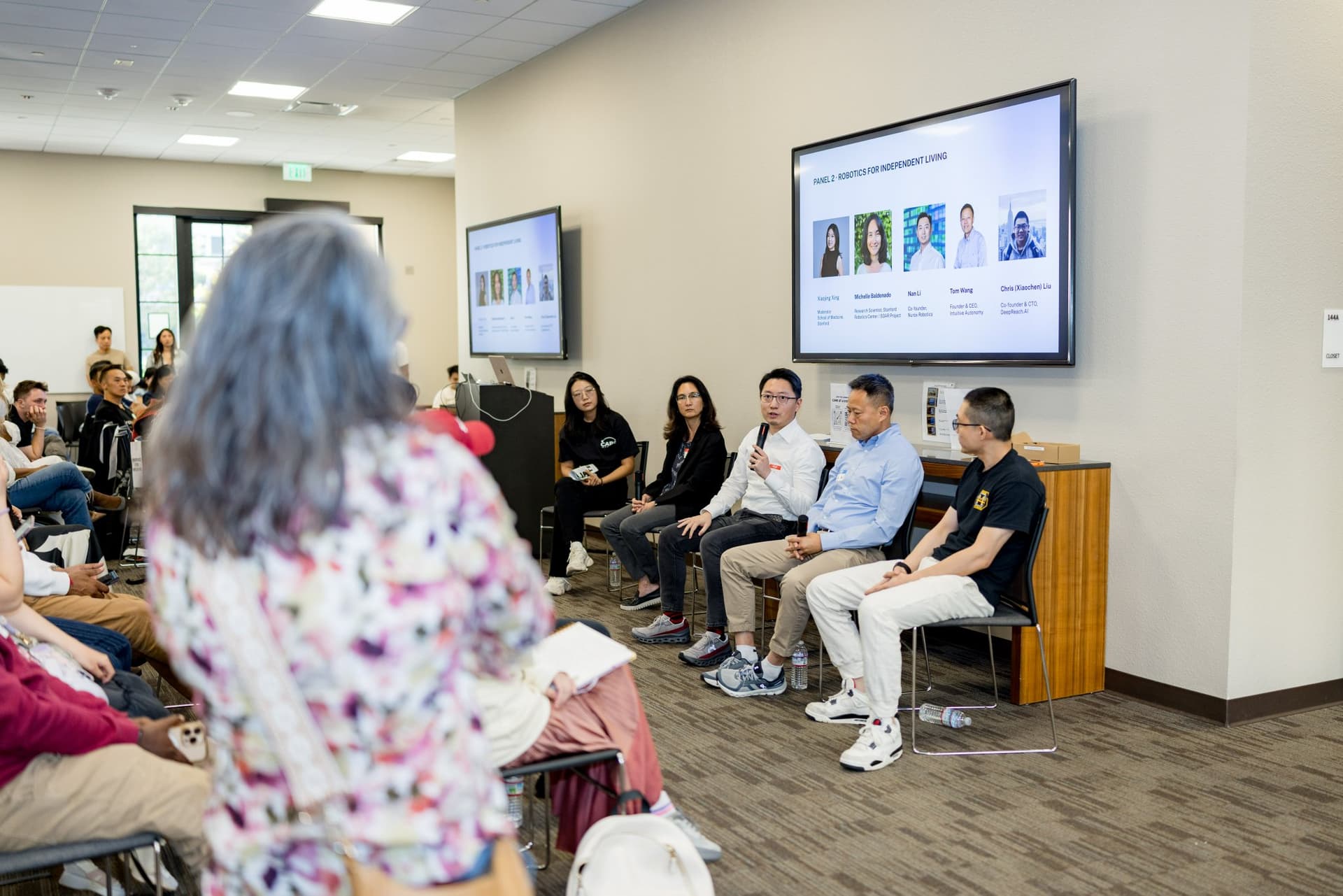 Audience member asking a question facing the Panel 2 "Robotics for Independent Living" panelists at Care at a Distance: AI, Sensors, Robotics and the Future of Aging, SF Tech Week 2026 at EVGR, Stanford University by JY Studio