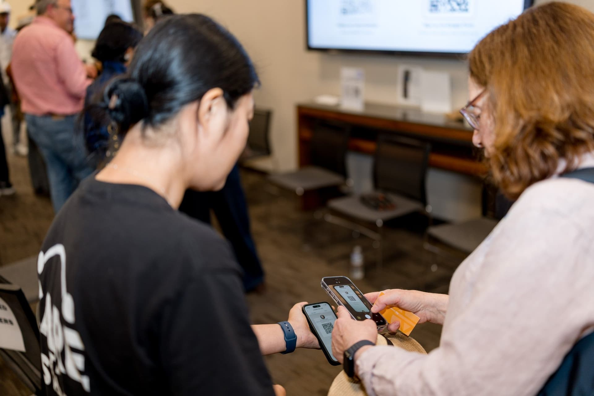 Two attendees exchanging contacts on their phones during networking at Care at a Distance: AI, Sensors, Robotics and the Future of Aging, SF Tech Week 2026 at EVGR, Stanford University by JY Studio