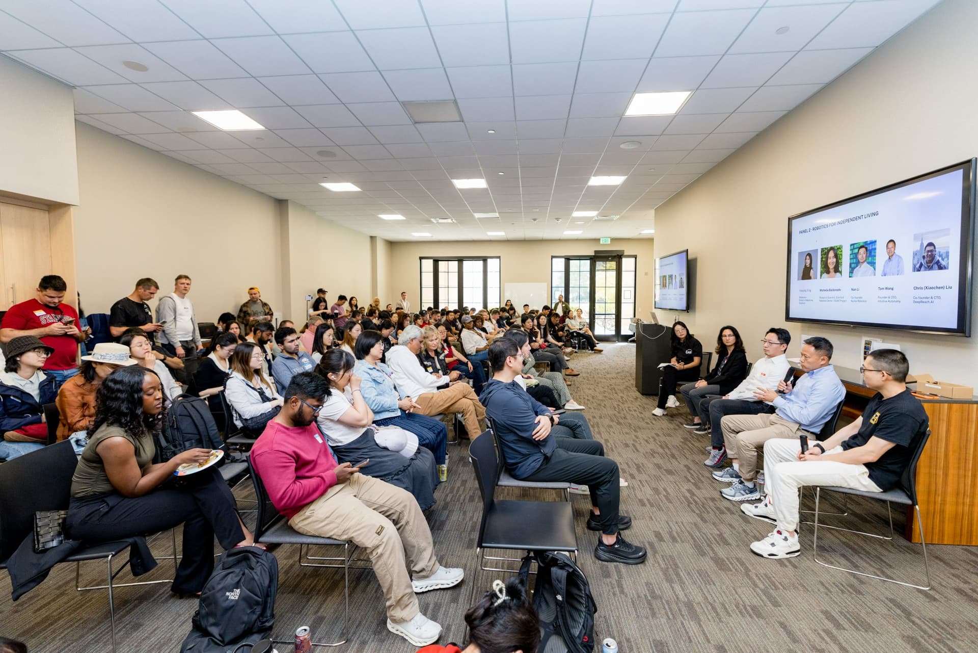 Wide angle of the Panel 2 "Robotics for Independent Living" panelists and the full audience at Care at a Distance: AI, Sensors, Robotics and the Future of Aging, SF Tech Week 2026 at EVGR, Stanford University by JY Studio