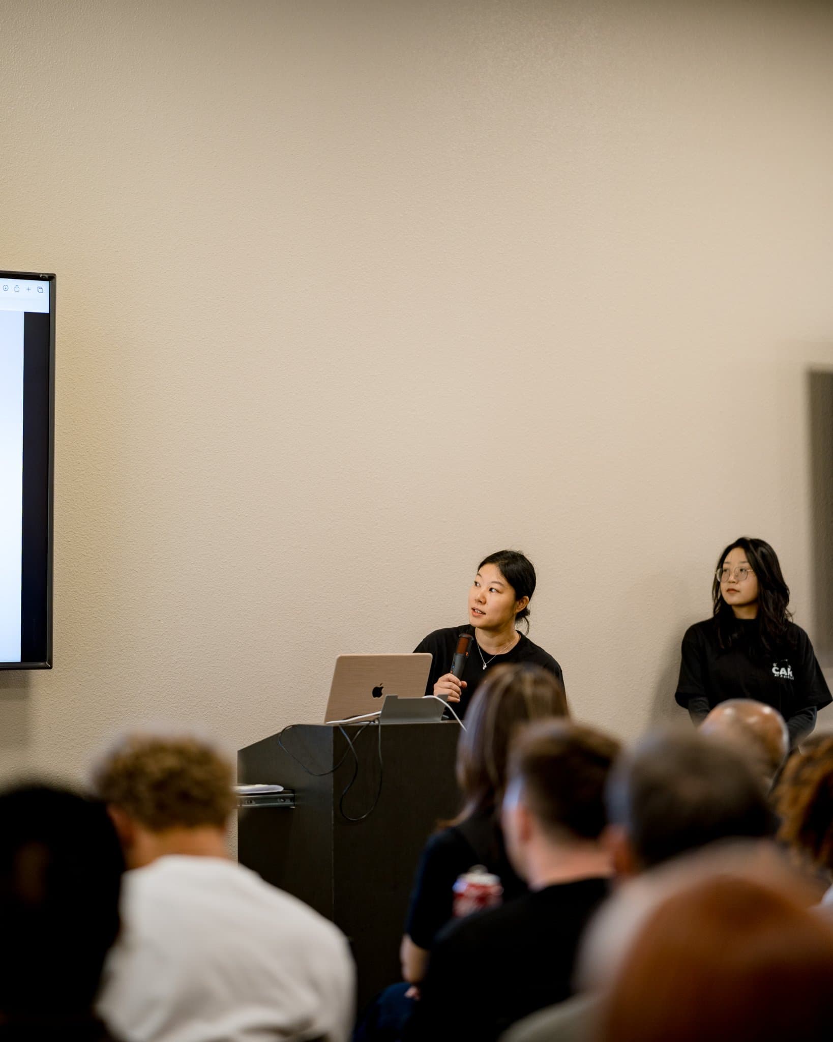 Vertical shot of the two event hosts at the podium at Care at a Distance: AI, Sensors, Robotics and the Future of Aging, SF Tech Week 2026 at EVGR, Stanford University by JY Studio