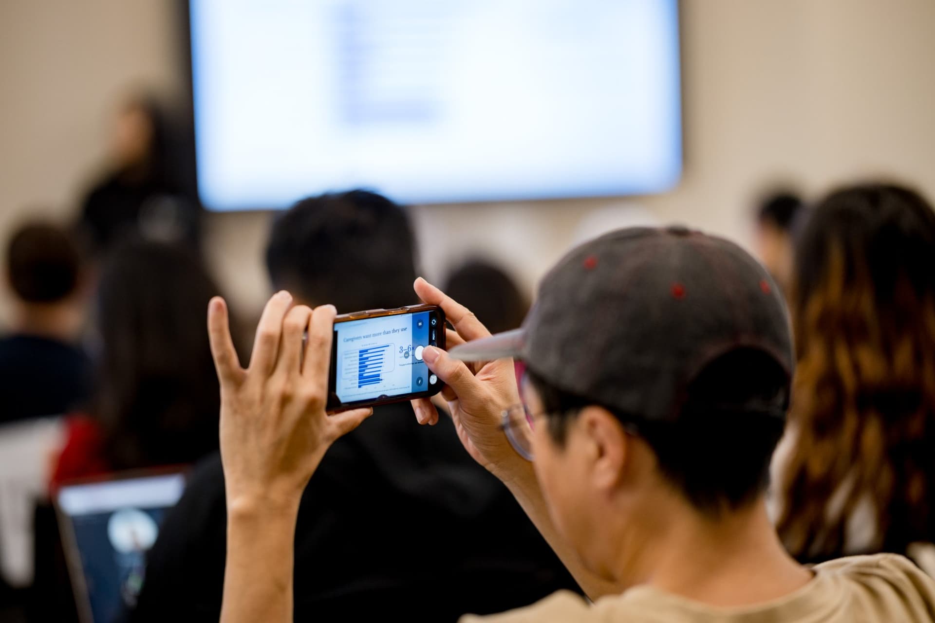 Attendee photographing the presentation slide on a phone at Care at a Distance: AI, Sensors, Robotics and the Future of Aging, SF Tech Week 2026 at EVGR, Stanford University by JY Studio