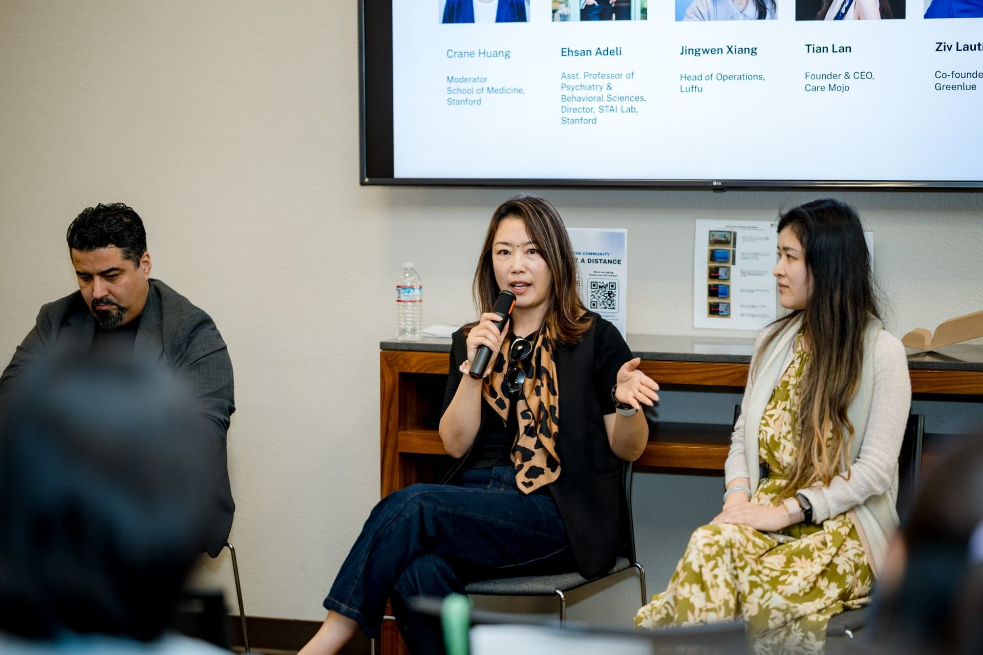 Two panelists of Panel 1 "Sensing Wellbeing from a Distance" speaking with a microphone at Care at a Distance: AI, Sensors, Robotics and the Future of Aging, SF Tech Week 2026 at EVGR, Stanford University by JY Studio