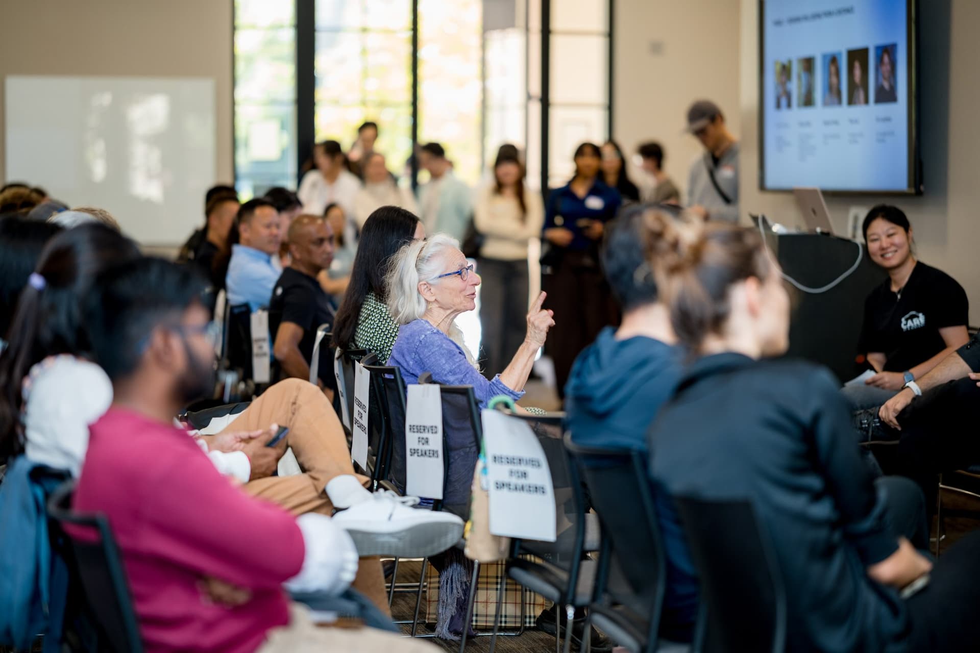 Audience and panel seen from the side with the speaker slide on screen at Care at a Distance: AI, Sensors, Robotics and the Future of Aging, SF Tech Week 2026 at EVGR, Stanford University by JY Studio