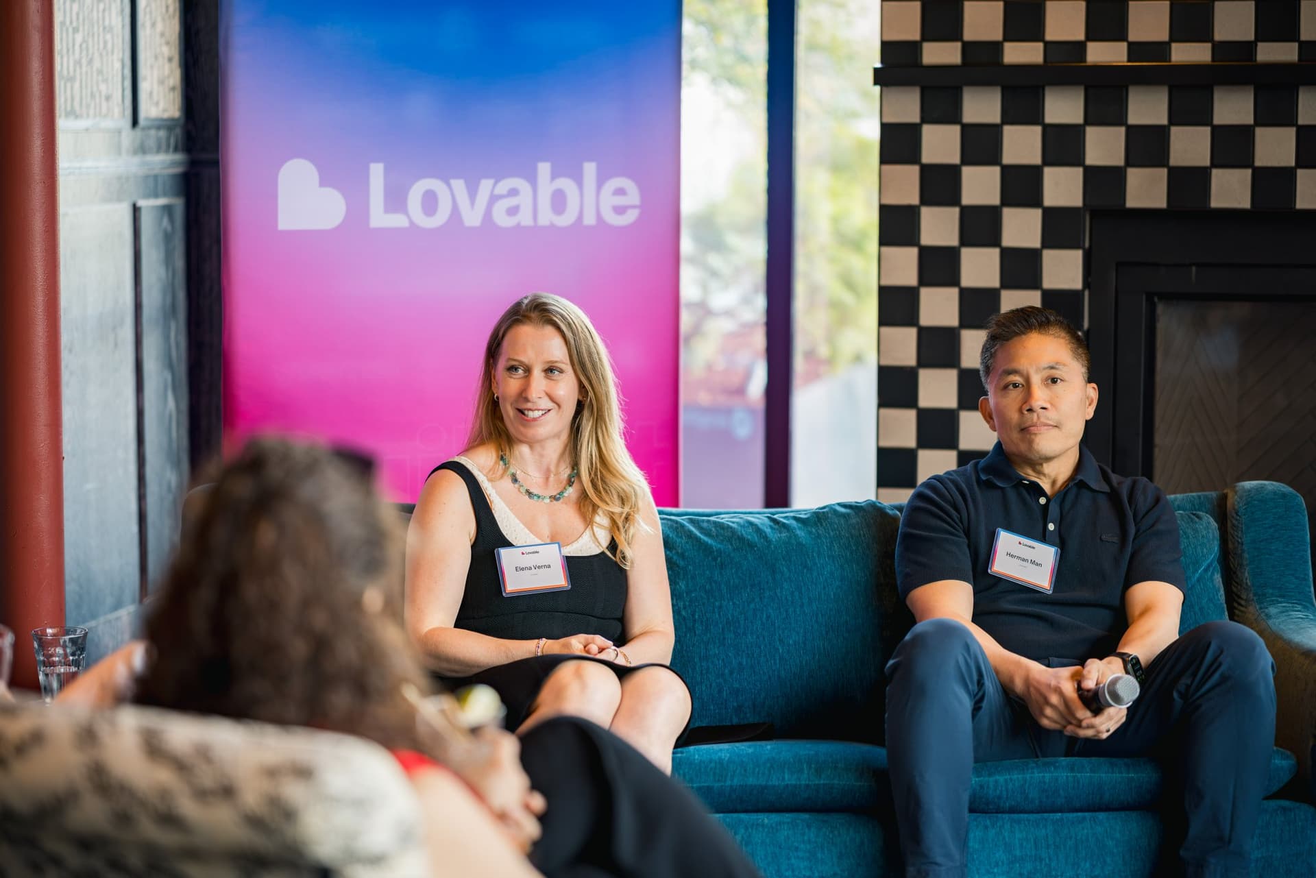 Panelists Elena Verna of Lovable and Herman Man of Ironclad on the teal sofa in front of the Lovable banner at Lovable's When Everyone Can Build panel in San Francisco by JY Studio