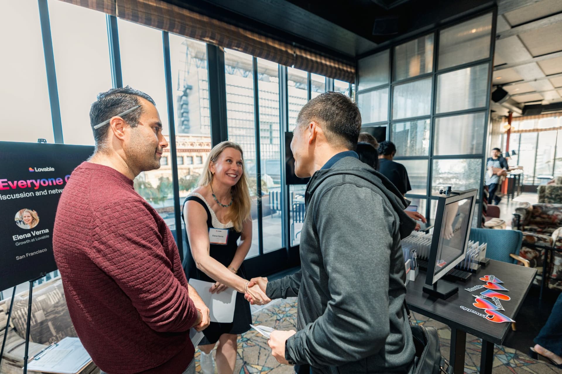 Panelists greeting a guest with a handshake beside the event sign at Lovable's When Everyone Can Build panel in San Francisco by JY Studio