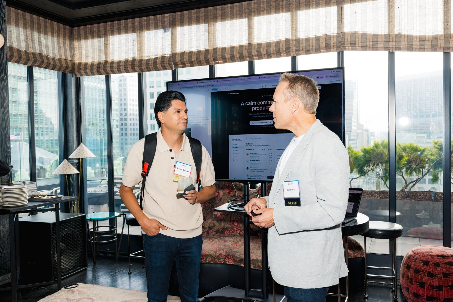 Two guests chatting beside a product demo screen with city views at Lovable's When Everyone Can Build panel in San Francisco by JY Studio