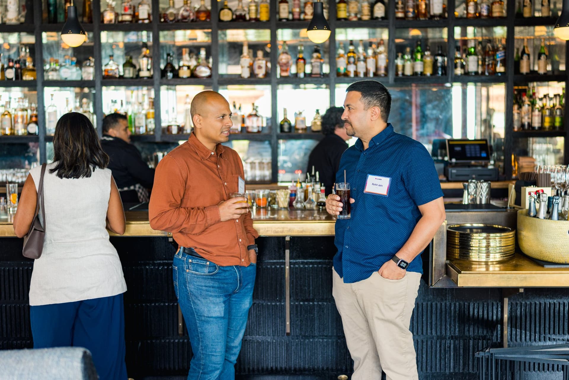 Guests chatting with drinks in front of the backlit bar at Lovable's When Everyone Can Build panel in San Francisco by JY Studio
