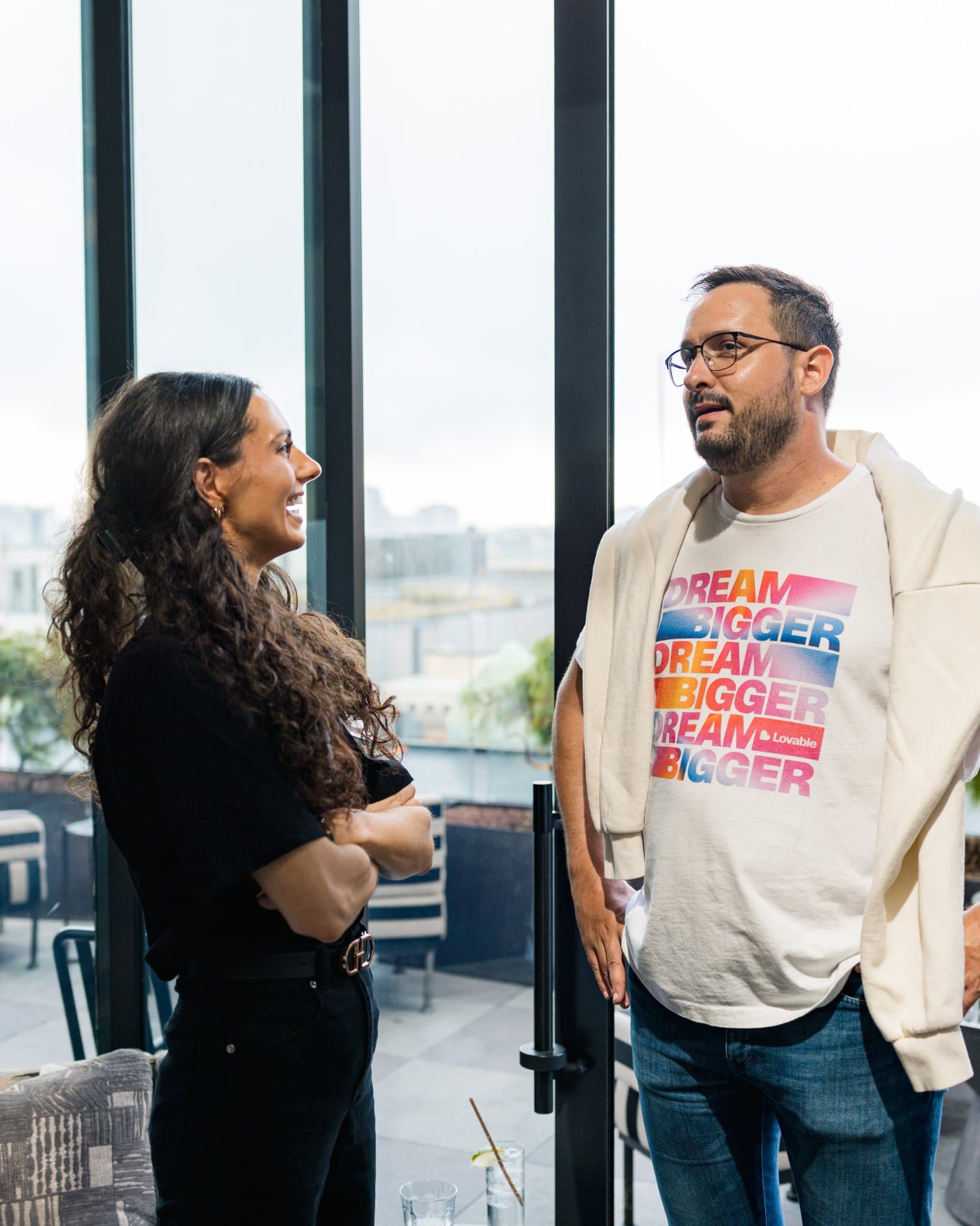 Guest in a Lovable Dream Bigger t-shirt chatting by the windows at Lovable's When Everyone Can Build panel in San Francisco by JY Studio