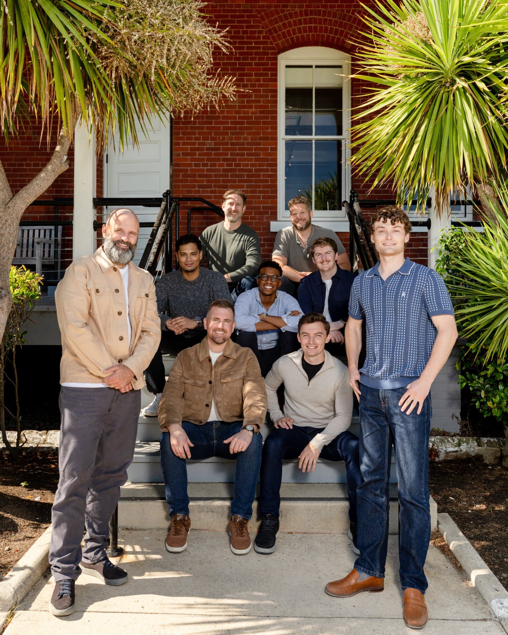 General Compute AI startup full team group photo on the front steps of a red-brick building with palm trees in natural sunlight, vertical on-site team photography in San Francisco for About page, LinkedIn and fundraising announcements by JY Studio